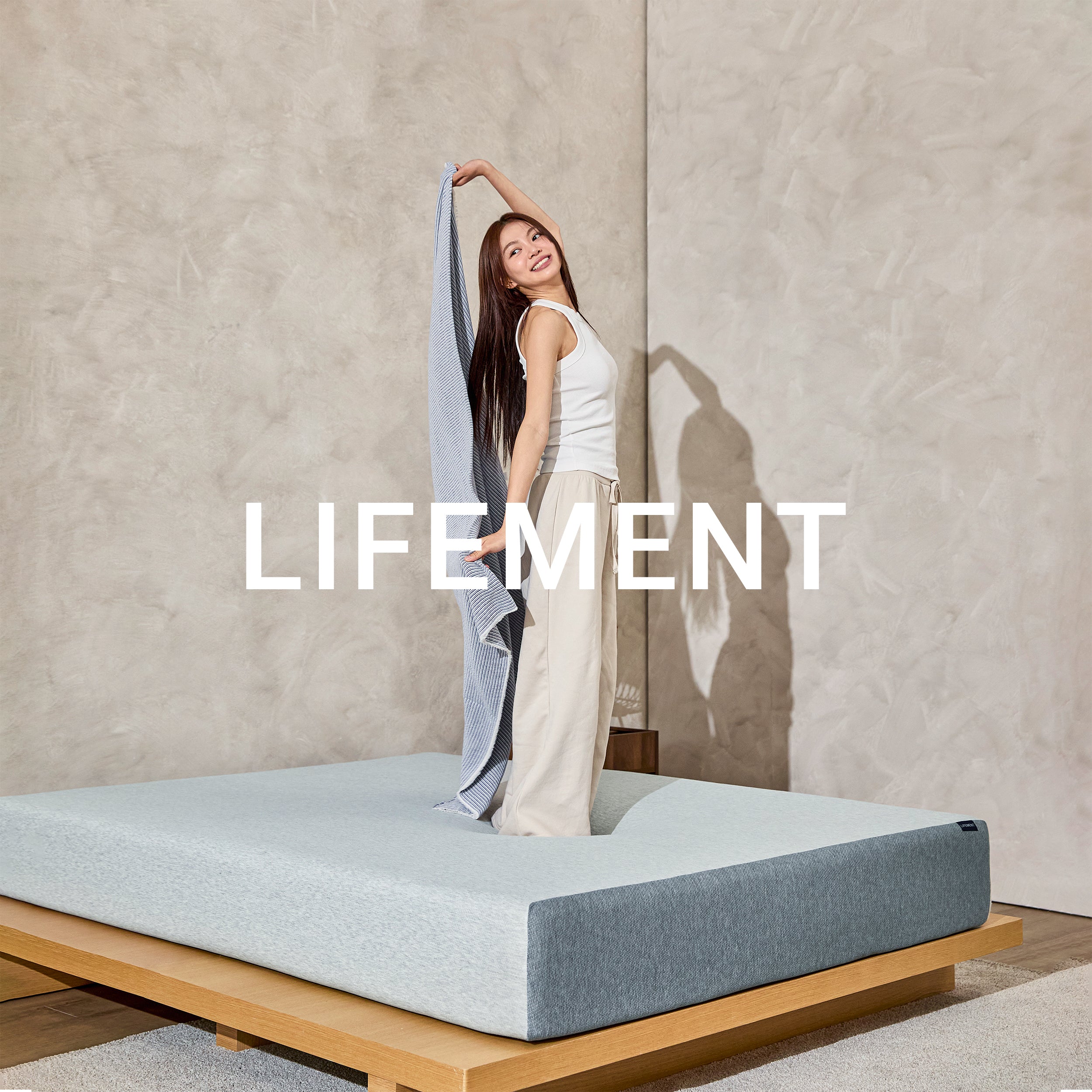 Woman standing on a Lifement Basic Graphite Memory Foam Mattress in a bright room with Lifement branding