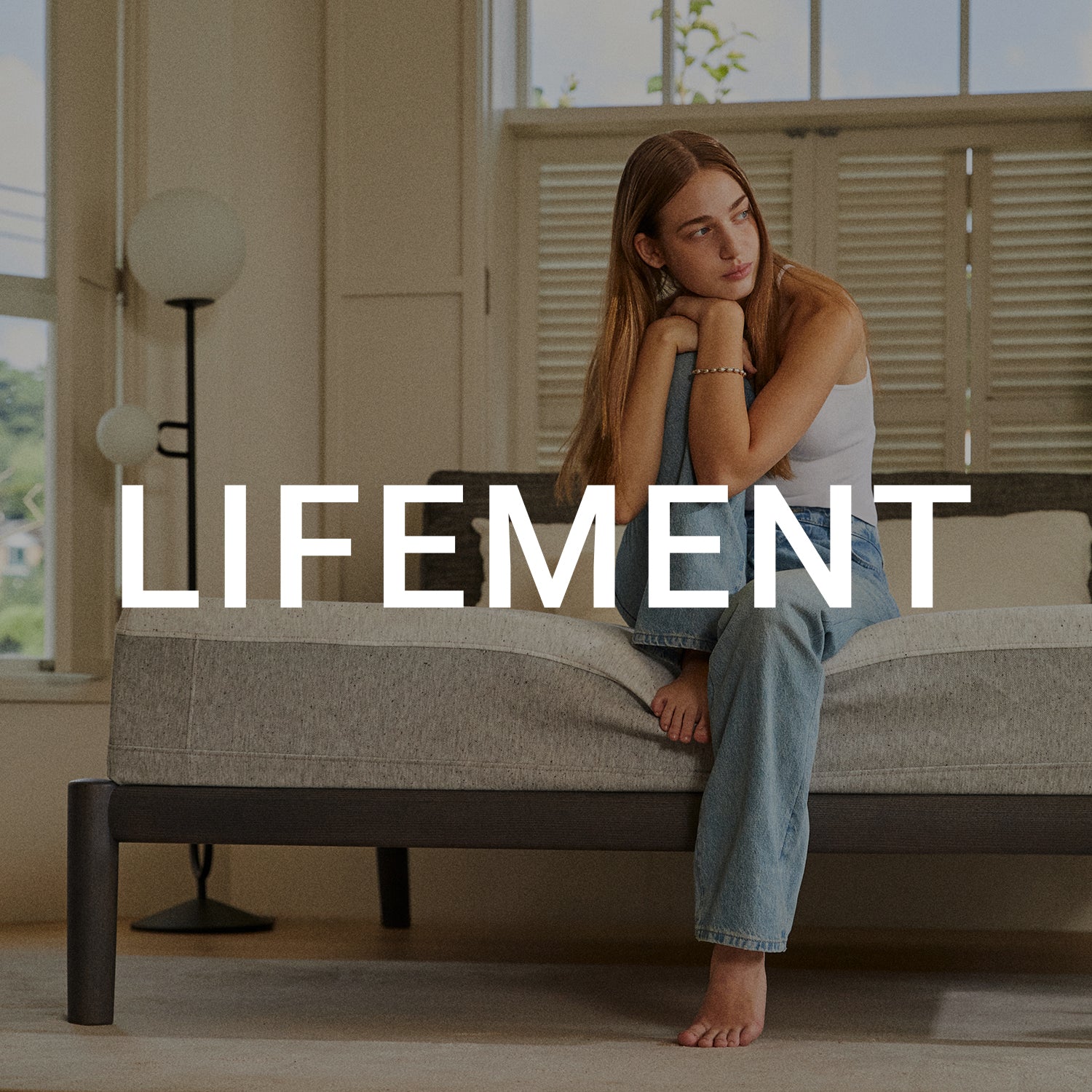 Woman resting comfortably on a Lifement mattress in a bright, airy bedroom with natural light