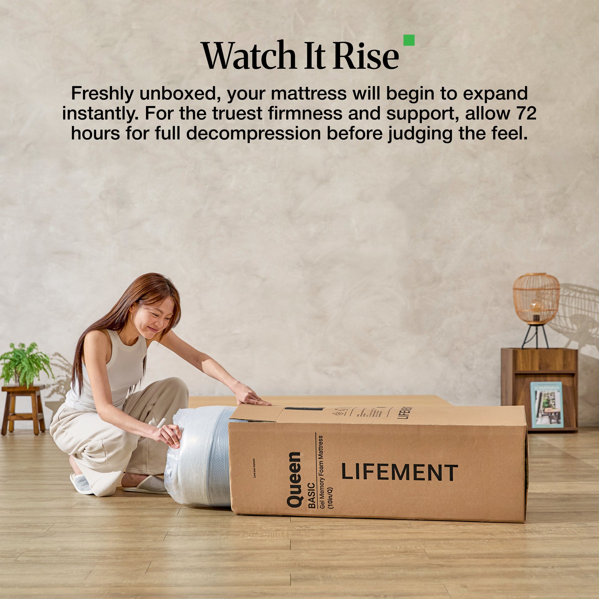 Woman sitting beside a boxed Lifement mattress demonstrating mattress-in-a-box expansion with 72-hour decompression guidance