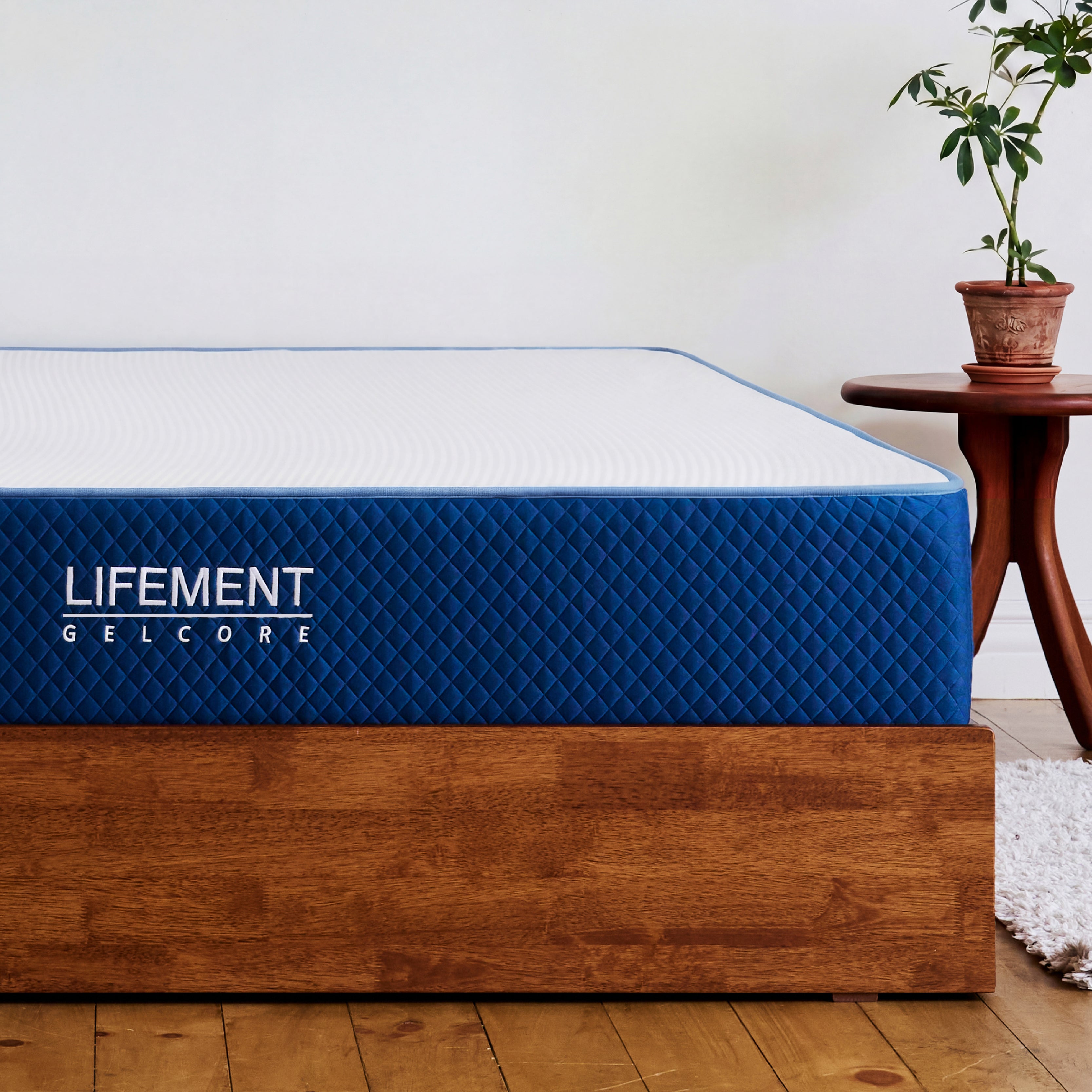 Lifement Gel Core Grid Mattress with blue quilted cover and branded side panel on a wood bed frame in a bedroom with plant decor