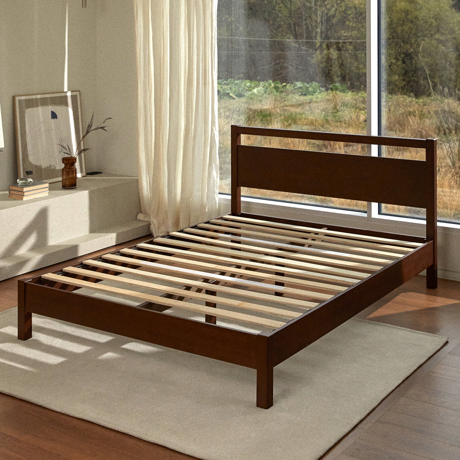 A sunlit room with walnut colored wood bed fame with headboard. There is no mattress to reveal the wooden slats